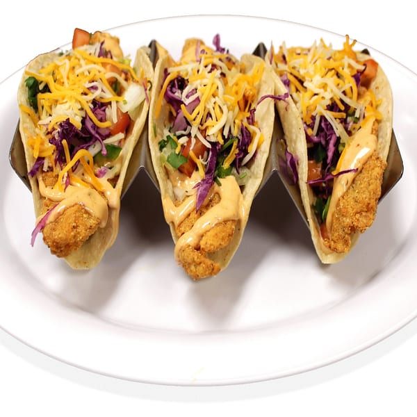 Three tacos with crispy fried protein, shredded cheese, red cabbage, and creamy sauce on a white plate.